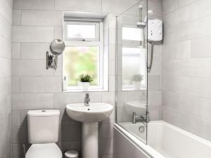 a white bathroom with a sink and a toilet and a window at Seashell Cove in Cemaes Bay