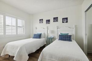 two beds in a white room with blue pillows at Sunrise at the Beach - 2BR Apt with Scenic Views in Satellite Beach