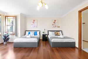 two beds in a white room with wood floors at Quadruple Room w Ensuite in Gordon near Train & Bus in Pymble