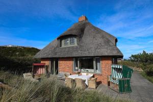 a thatch roofed house with a table and chairs at Strandhaus Höltig in Hörnum