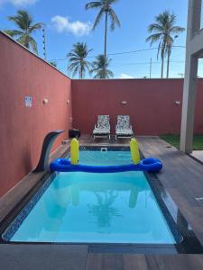 a small swimming pool with two chairs next to a red wall at Casa de férias ventilada com 4 quartos à 5 min da praia in Salinópolis