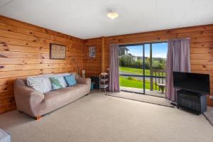 a living room with a couch and a flat screen tv at Bay View Bach - Langs Beach Holiday Home in Waipu