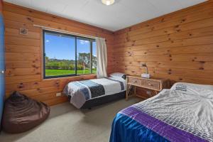 twee bedden in een kamer met houten wanden en een raam bij Bay View Bach - Langs Beach Holiday Home in Waipu