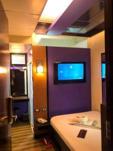 a bedroom with a purple wall with a tv on the wall at Harimariz Dormitory Official in Dumaguete