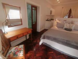 1 dormitorio con cama, escritorio y espejo en Beulah Lodge en Ciudad del Cabo