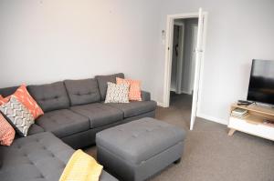 a living room with a gray couch and a ottoman at Nights on Broadway - THE HOUSE in Matamata