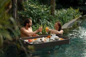 a man and woman sitting in the water with drinks at The Lokha Ubud Resort, Villas & SPA in Ubud