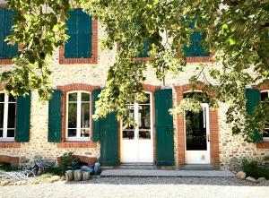 un edificio con persianas verdes y una puerta blanca en Sous le Tilleul de la Condomine, grand gite piscine privee, en Payrin-Augmontel