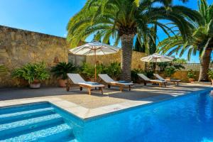 una piscina con sillas, sombrillas y palmeras en Villa Can Raco Ibiza, en Sant Rafel de sa Creu