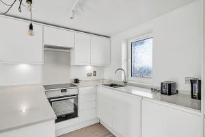 cocina blanca con armarios blancos y ventana en Radiant Chelsea Flat with City View, en Londres