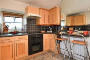 a kitchen with wooden cabinets and black appliances at Beautiful cottage a stones throw from the beach. in Llanbedrog
