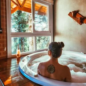 a woman sitting in a bath tub with a window at Chalés Descanso na Serra in Monte Verde