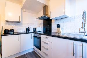 a kitchen with white cabinets and a black counter top at Redcroft Green - Modern 3 bedroom house in Kenton