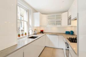 uma cozinha branca com armários brancos e um lavatório em Lovely Central Apartment with Park Views em Londres