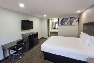 a hotel room with a bed and a desk and a television at Travelodge by Wyndham Buena Park in Buena Park