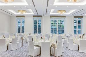 een kamer met witte tafels en stoelen en kroonluchters bij Dorint Parkhotel Meißen in Meißen