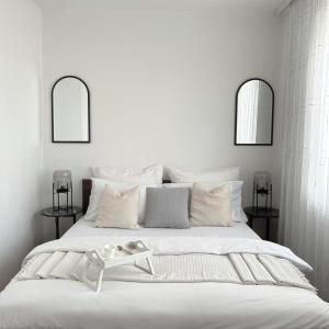 een witte slaapkamer met een groot wit bed en 2 spiegels bij Bright Prishtina City Apartment in Pristina