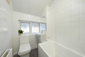 a white bathroom with a toilet and a window at Modern Two Bedroom Flat with Free Parking Near Heathrow in Feltham