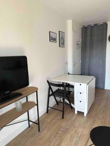 een woonkamer met een bureau, een tv en een tafel bij Le Balbec - Appartement Cosy in Cabourg