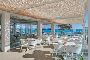 um restaurante com mesas e cadeiras brancas e o oceano em The Sea Hotel by Grupotel - Adults Only em Can Picafort