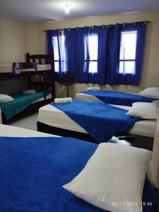 Cet appartement comprend une chambre dotée de 3 lits avec des draps bleus et des fenêtres. dans l'établissement Pousada Diamante da Serra, à Areia