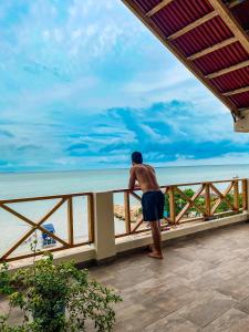 a man standing on a balcony looking at the ocean at Merakai Hostel Rincon del Mar in Rincón