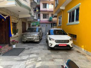 dois carros estacionados ao lado de um edifício amarelo em Boudha Dungkar guest house em Kathmandu