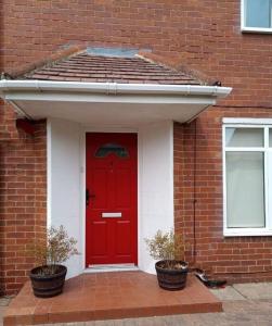 a red door on a brick building with two plants at Beside the Seaside Tynemouth in Cullercoats