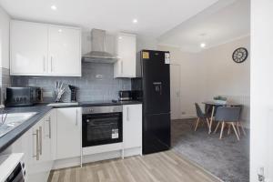 eine Küche mit weißen Schränken und einem schwarzen Kühlschrank in der Unterkunft Spacious Living Room & Modern Comforts, Sleeps 4 in Peterlee