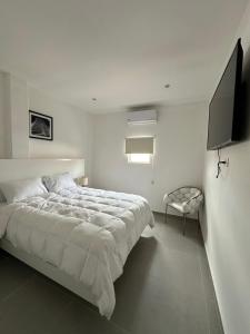 a white bedroom with a bed and a flat screen tv at Cantares Adults Only in Cancún