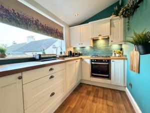 una cocina con armarios blancos y una ventana en Chestnut Cottage, en Dalmellington