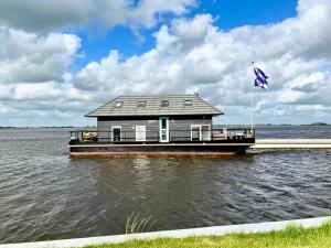 una casa flotante en el agua con bandera en Het VaarHuis - Beachclub Sneek, en Offingawier