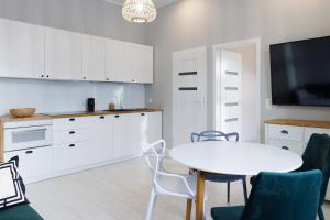 a kitchen with white cabinets and a white table and chairs at Apartament Piotrkowska 67 Primo in Łódź