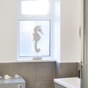 ventana con decoración de caballito de mar en el baño en Avocet Cottage Amble, en Amble