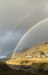 a rainbow over a field with houses and a river at Cosy groundfloor apartment in Sørvágur