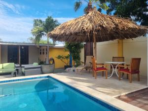 een zwembad met een tafel en een rieten parasol bij Aruba SeaScape Apartments in Palm-Eagle Beach