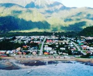 a town on a beach with mountains in the background at Arrayan The Cuyen in Puerto Cisnes