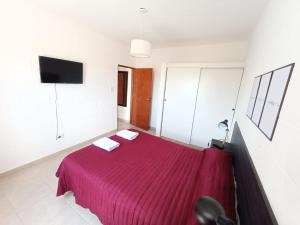1 dormitorio con 1 cama roja y 2 toallas blancas en Departamentos Universidad en Río Cuarto