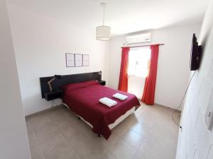 1 dormitorio con 1 cama roja y 2 toallas en Departamentos Universidad en Río Cuarto