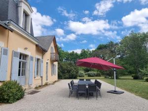a table and chairs with a red umbrella at Luxe et tranquillité au vert: maison 6 chambres, piscine, proche du Mans, idéale familles et groupes - FR-1-410-361 in Parigné-lʼÉvêque