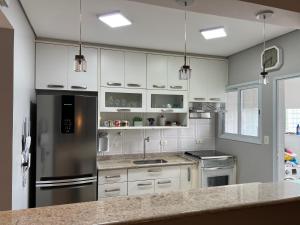 a kitchen with white cabinets and a stainless steel refrigerator at Apto beira mar pé na areia in Caraguatatuba