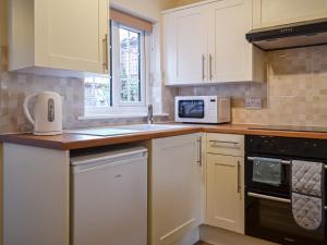cocina con armarios blancos y microondas blanco en End Cottage, en Horncastle