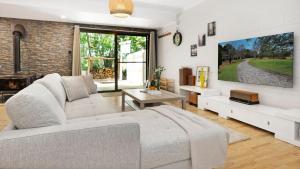 a living room with a couch and a tv on a wall at Fern Creek Cottage in Berrima