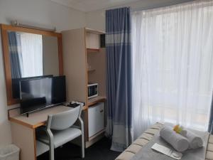Habitación de hotel con escritorio, cama y TV en Forstay Motel en Forster
