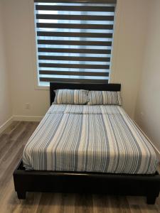 a bed with a striped comforter in front of a window at Panel Apartment in Winnipeg