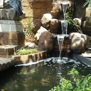 a water fountain in a garden with a pond at Caniga Hotel Yogyakarta in Gondowulung