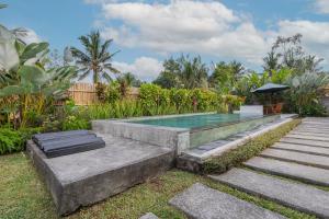a swimming pool in a garden with a table and an umbrella at Kubu Selat Villa and Glamping in Gianyar