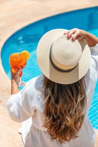 een vrouw met een hoed en een drankje naast een zwembad bij Meliá Lloret de Mar in Lloret de Mar