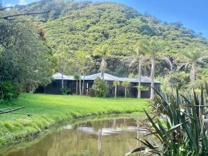 a house next to a river with a mountain in the background at The Bungalow in Great Barrier Island
