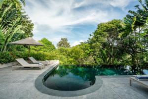 - une piscine avec 2 chaises et un parasol dans l'établissement Noku Phuket, à Chalong